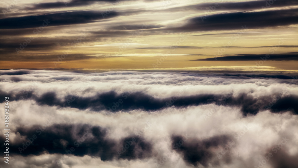 Obraz premium Dramatic layered clouds forming atmospheric cloud inversion above landscape at sunrise