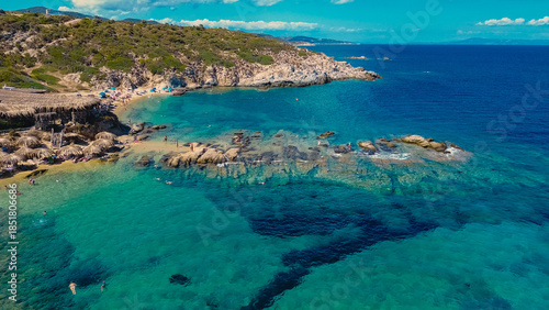 People enjoy a sunny day at a beautiful wild beach in Greece, surrounded by turquoise waters, sandy shores, and rocky formations perfect for a relaxing vacation.