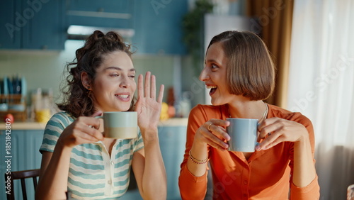 Bild auf Leinwand Two sisters gossiping kitchen holding coffee cups closeup