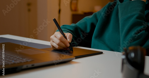 Female graphic designer focusing intently on photo retouching, using graphics tablet while working comfortably from home studio during evening hours
