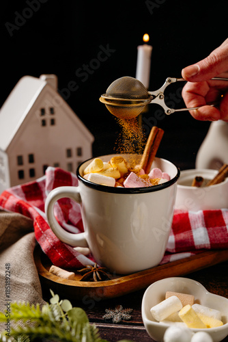 Hands adding topping to hot cocoa with marshmallows on cozy winter table. Warm holiday drink preparation and home comfort lifestyle moment.