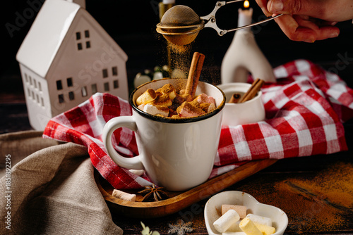 Hands adding topping to hot winter drink with cookies and festive decor. Cozy holiday cooking moment and home comfort lifestyle.