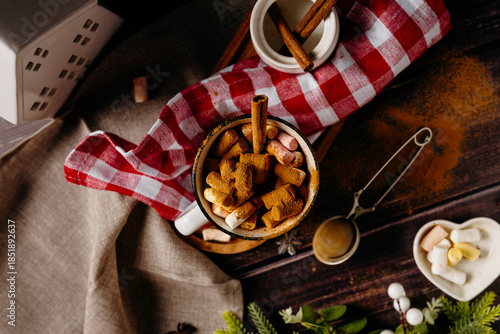 Winter still life with bowl of cookies, hot drink and cinnamon sticks. Cozy holiday food styling and warm seasonal atmosphere.