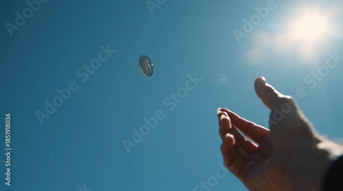 Coin in the Air: An individual extends a hand towards a coin suspended mid-air against a vibrant blue sky, inviting a sense of chance and anticipation. 