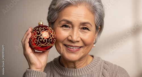 Elderly Asian woman smiling while holding Christmas ornament  