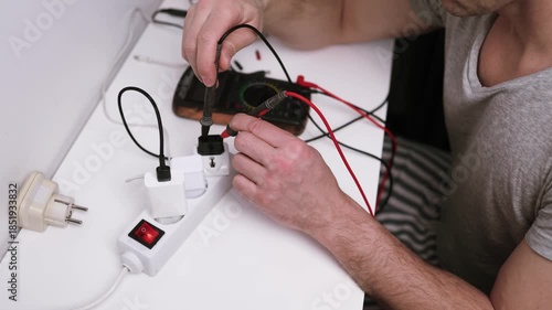 Close up on hands of caucasian man electrician using multimeter working on the plug electric or extension power strip, electric socket.