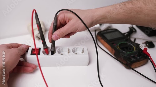 Close up on hands of caucasian man electrician using multimeter working on the plug electric or extension power strip, electric socket.