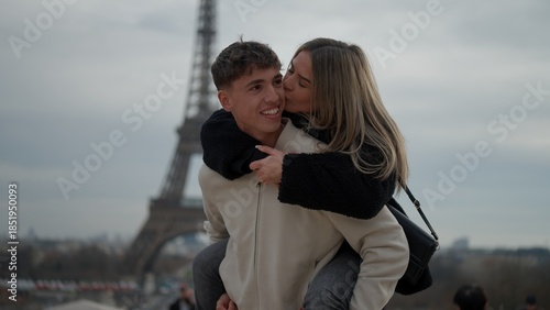 A romantic couple enjoys a piggyback ride in Paris France with the Eiffel Tower in the background The woman kisses the man showcasing love and affection in this travel photography scene.