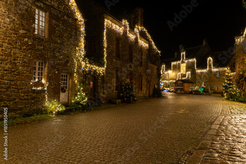 Rue du village de Locronan en Bretagne décorée de guirlandes lumineuses pour les fêtes de Noël, maisons en pierre et ambiance nocturne chaleureuse dans un village breton.