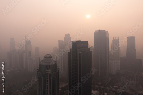Aerial view of the Jakarta skyline obscured by thick smog and air pollution during sunrise, highlighting the city's environmental and air quality challenges