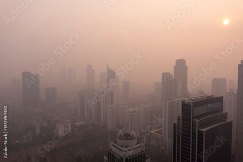 Aerial view of the Jakarta skyline obscured by thick smog and air pollution during sunrise, highlighting the city's environmental and air quality challenges