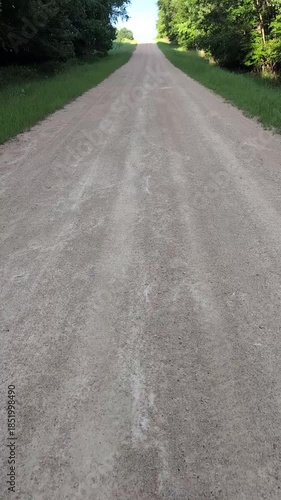 POV vertical walk down a peaceful gravel road lined with lush green spring trees. Immersive hiking perspective with natural footstep sounds.