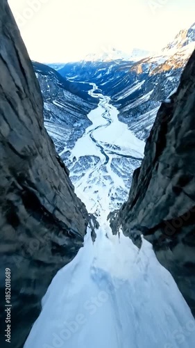 Steep snowy canyon walls frame a winding frozen river through distant mountains