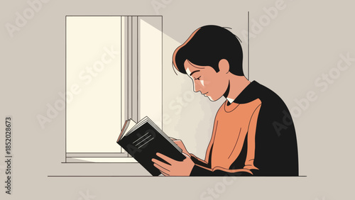 Young man engrossed in reading a book by the window bathed in natural light.