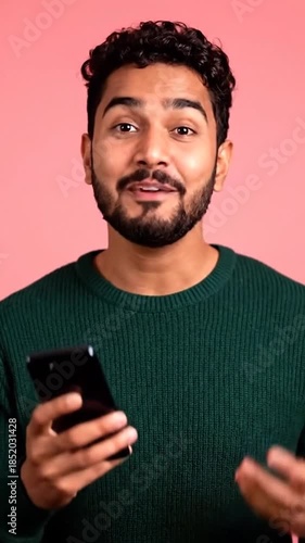 Smiling man with dark hair and beard, wearing a green sweater, holding a smartphone