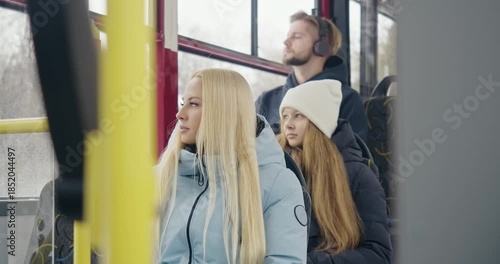 Side view of passengers going home by bus. Blonde woman sitting, young girl in white hat looking in window, boy with earphones listening to music. Concept of public transport.