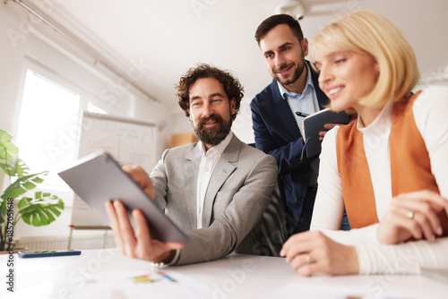 Картината върху платно Group of professionals collaborates and shares ideas on a tablet in a bright office space