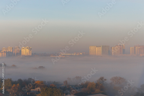 Tender sunrise over the city. Gradient morning sky over city in fog. Morning haze in downtown, high angle view. Misty cityscape with copy space. Autumn landscape in town. 