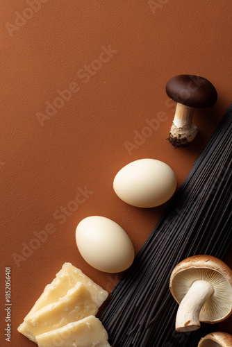 Ingredients for cooking mushroom pasta on a brown background. Black spaghetti, mushrooms, eggs, and parmesan cheese arranged with copy space.