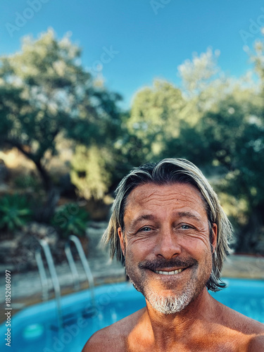 Happy blond man with a stubble beard by a pool in a sunny summer garden.