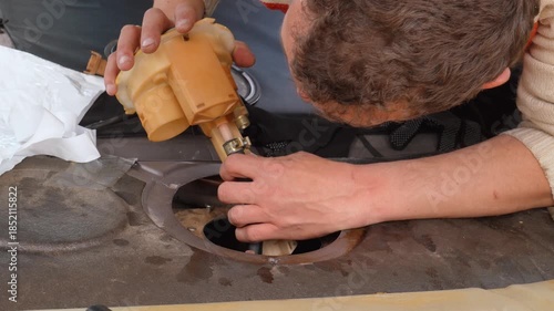 Automotive technician carefully installing a new fuel pump assembly into the gas tank of a modern vehicle during a repair service in a garage, showcasing a complex maintenance procedure
