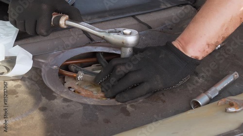 Professional auto mechanic wearing black gloves disassembling and replacing the car fuel pump module during a vehicle maintenance service at the garage, demonstrating a complex repair process