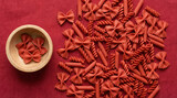 Red pasta assortment on textured background with wooden bowl