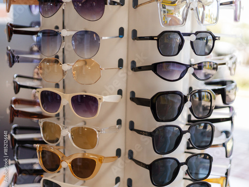 Many styles of sunglasses are arranged on a display stand in a retail store. The sunlight shines on the glasses, attracting customers to browse and shop