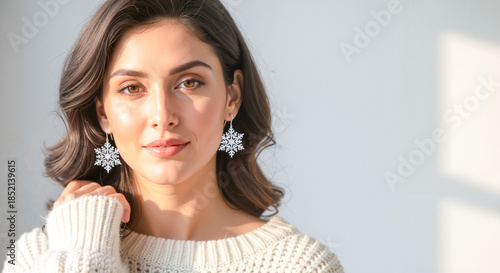 Woman wearing snowflake earrings while smiling in cozy sweater, studio photo, copy space  