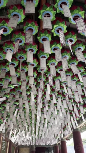 Colorful lotus lanterns with hanging paper wish tags decorating the ceiling of a traditional Buddhist temple corridor in South Korea