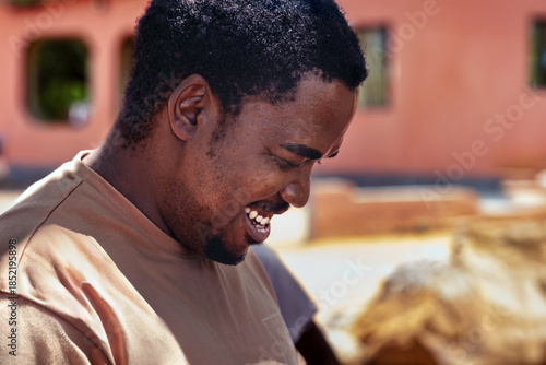 single young african man outdoors in the village, happy expression, enjoying a lough outside