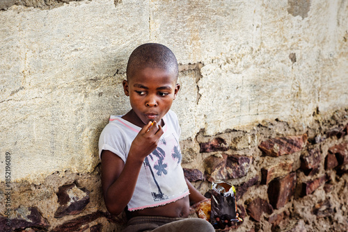 Tablou pe pânză hungry african girl child in the village, bald shaved head, , home next to the h