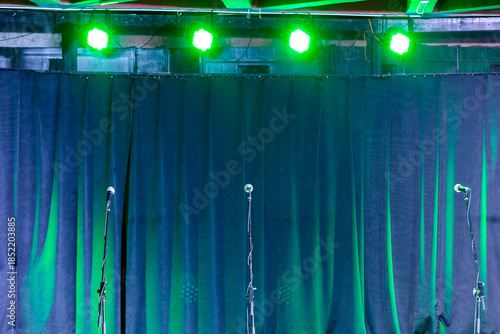 Microphones on stands on the stage against a background of curtains.