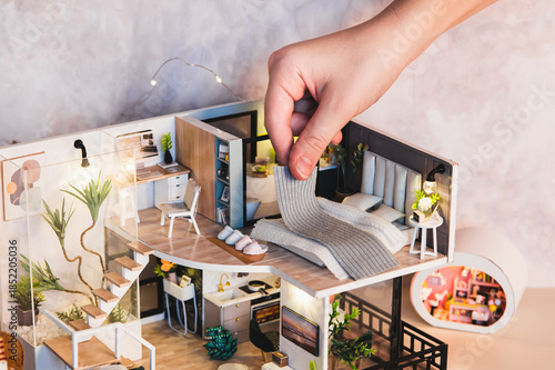 A child's hand puts a blanket on a bed on the second floor of a tiny house on a table