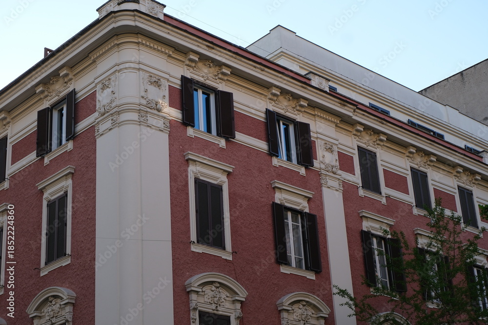 Naklejka premium Ornate building facade with symmetrical shuttered windows and textured pink stucco walls