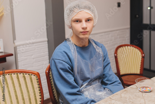 Фотография Portrait of a serious teenage boy wearing a white hairnet and transparent apron