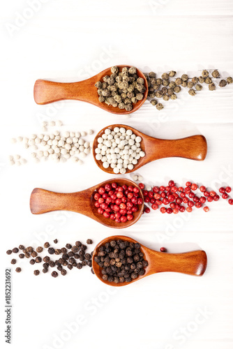spices, peppercorns of different colors, poured into four wooden spoons, on a white background
