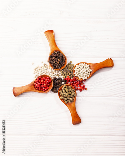four wooden spoons with spices, multi-colored peppercorns, on a white background