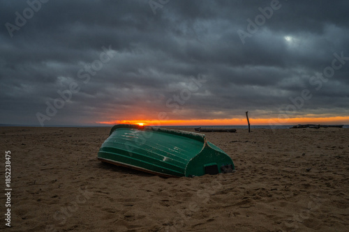 Green overturned boat on sandy beach at dramatic Baltic Sea sunset