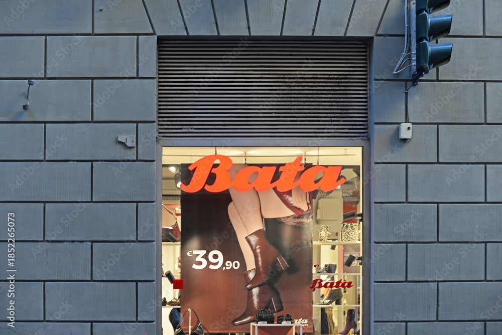 Naklejka premium SIENA, ITALY – OCTOBER 7, 2025: Bata shop window with orange logo and brown ankle boots for sale. The footwear and fashion accessories brand is headquartered in Lausanne, Switserland