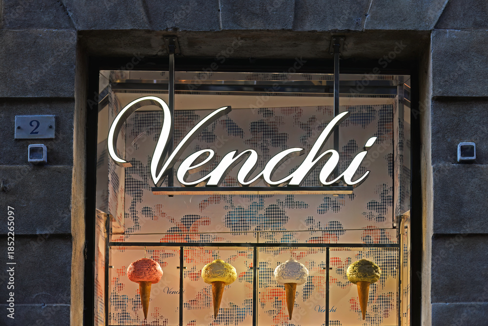 Naklejka premium SIENA, ITALY – OCTOBER 7, 2025: Venchi shop window with ice cones in different colours in antique building. Venchi is an Italian chocolate and gelato brand since 1878