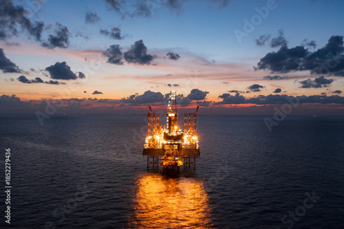 Aerial view from a drone of big jack up offshore drilling oil rig, production platform and supply vessel In the ocean during sunset - Oil and Gas Industry