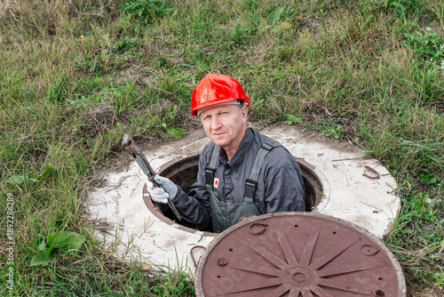 A plumber peers out from an open water well in a rural area. Plumbing repair and maintenance