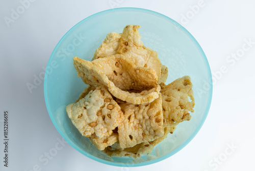 A top-down view of traditional Indonesian crispy crackers (krupuk) with visible seeds, served in a light blue plastic bowl against a plain white background.