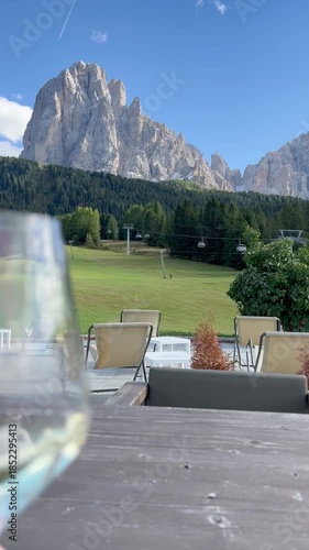 Relaxing moment at a mountain café in the Dolomites, Italy, during summer season. Seated viewpoint slowly revealing a glass of Italian wine enjoyed with a breathtaking alpine landscape