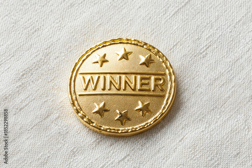 Shiny gold winner pin badge represents joyful victory success achievement. Round metal object symbolizes pride competition reward. Triumphant first place champion celebration on white texture
