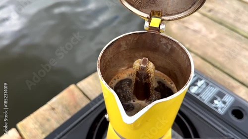 Making coffee on portable camping gas burner at lake. Brewing coffee outdoors on gas stove at lake. Espresso Maker. Moka Pot on Portable Gas Stove brews on wooden pier at river. Gas cooker travel.