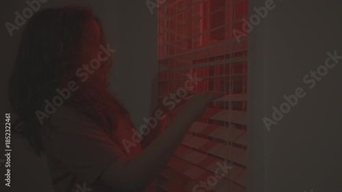 Kid unsafe at home night. Child dramatic portrait. Kid hiding behind window blinds at night. Child fear violence night interior. Child alone in darkness. Kid fear police emergency lights.