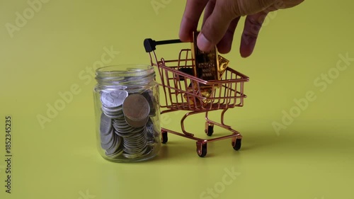 Hands putting gold into a shopping trolley beside which is a jar of coins