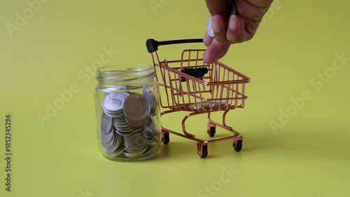 Hands inserting coins into a shopping trolley beside which there is a jar of coins